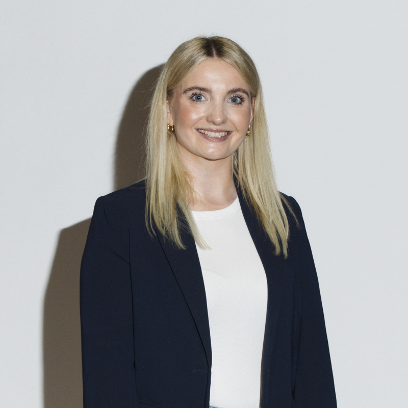 Frau mit blonden Haaren, die in einem schwarzen Blazer und einem weißen Oberteil gekleidet ist.