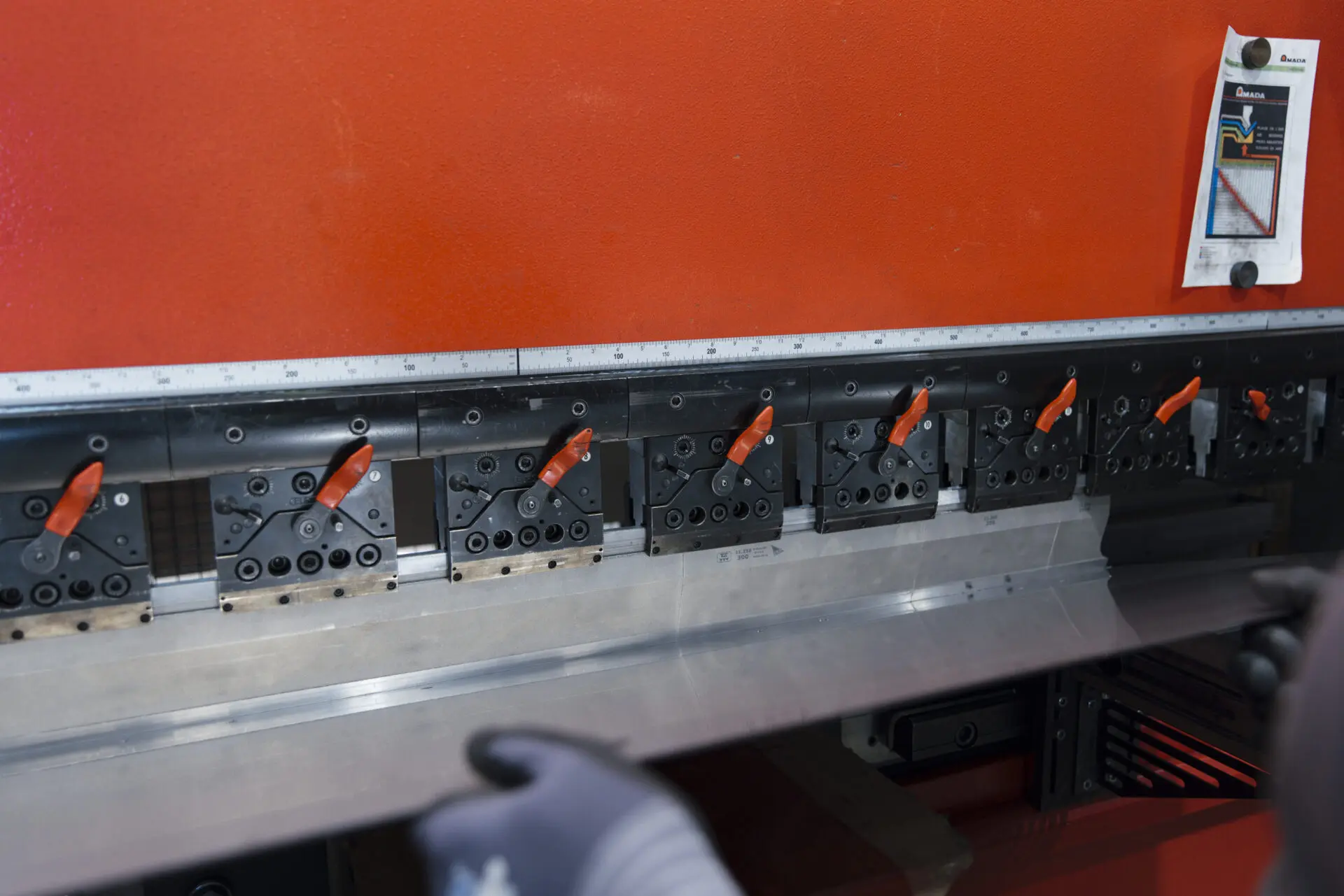 Biegemaschine mit verschiedenen Werkzeugen und einem Metallblech in den Händen eines Arbeiters.