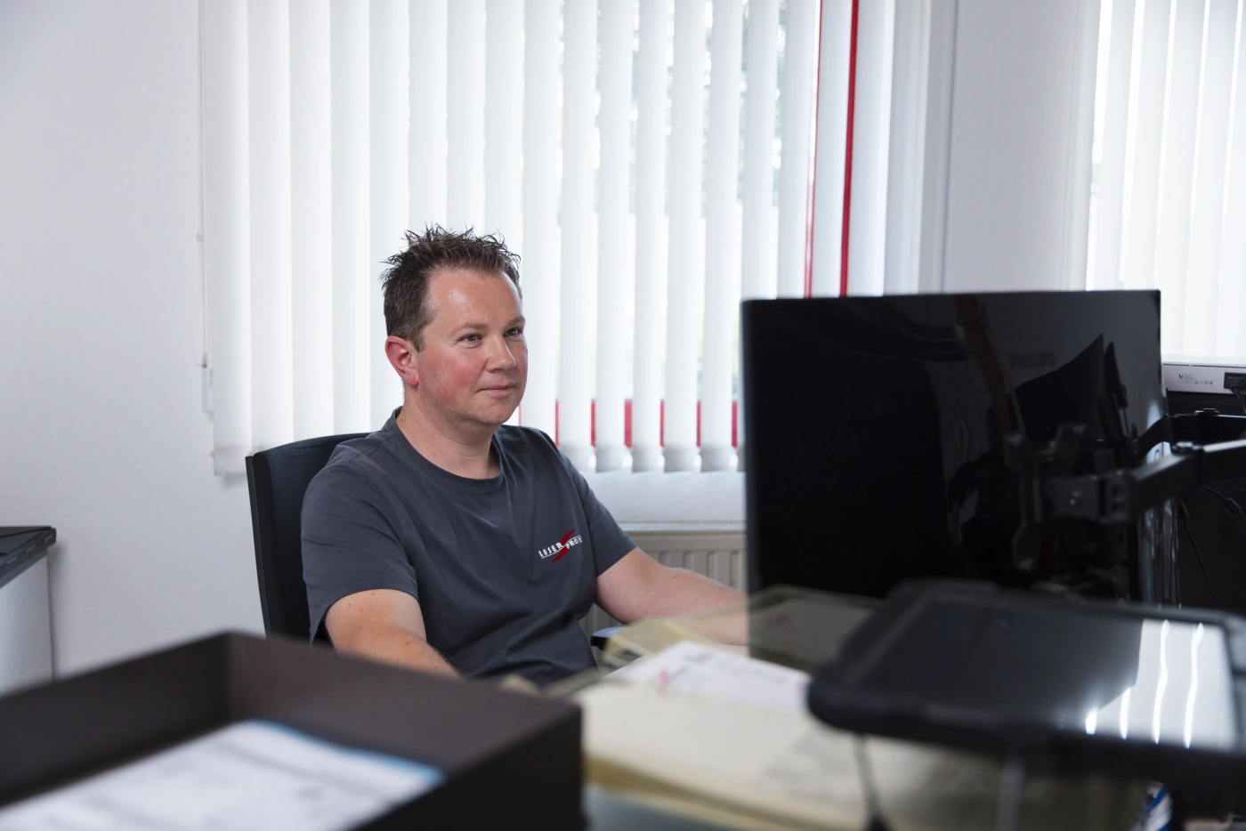 Mann mit kurzen Haaren sitzt an einem Schreibtisch vor einem Computerbildschirm im Büro.