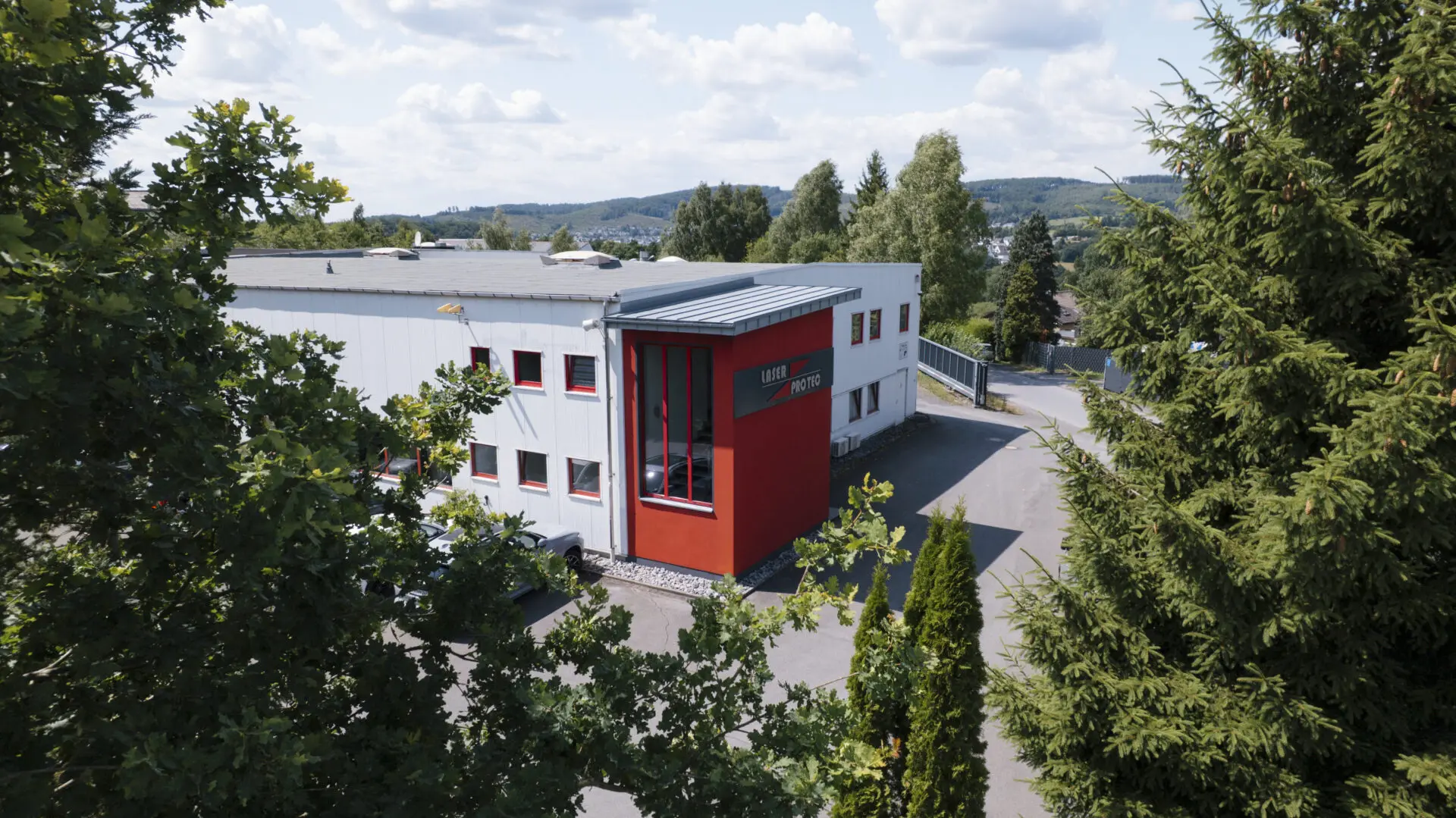 Das Gebäude von Laserprotec mit rotem und weißem Außenanstrich in einer ländlichen Umgebung.