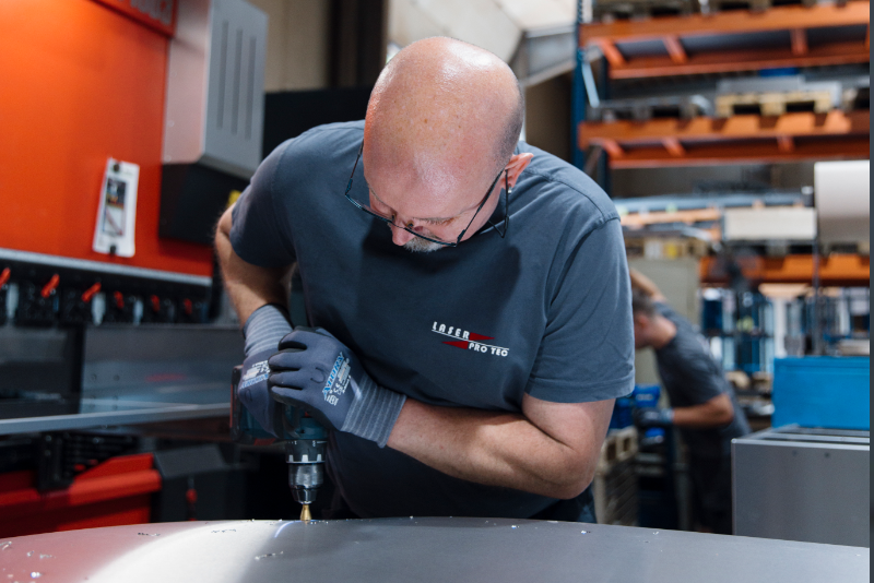 Mitarbeiter, der mit einer Bohrmaschine an einem Metallstück arbeitet in einer Werkstatt.