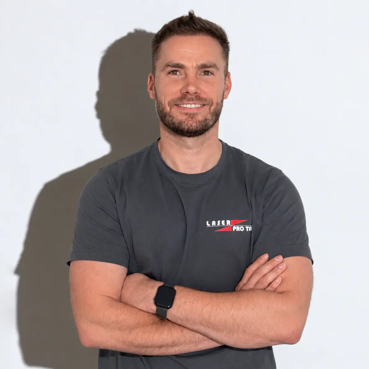 Mit verschränkten Armen lächelt Marc Rocholl im dunkelgrauen Laser Pro Tec T-Shirt und trägt eine schwarze Armbanduhr.